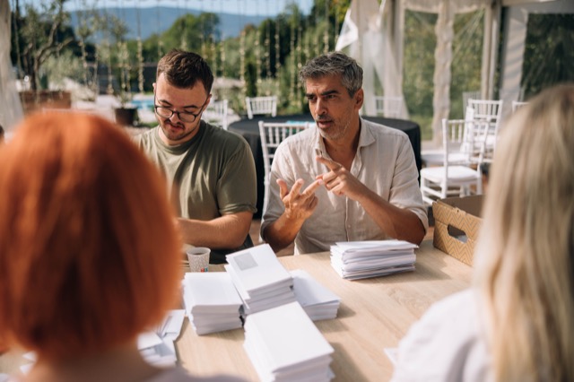 Bor Greiner z rokami razlaga sogovornikom za mizo na dogodku na prostem.